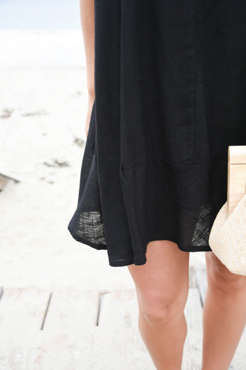 Black dress with sheer lace details on a blurred beach background