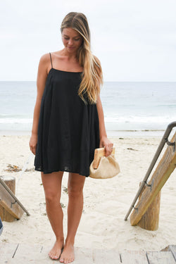 Woman in a black dress holding a beige bag on a beach