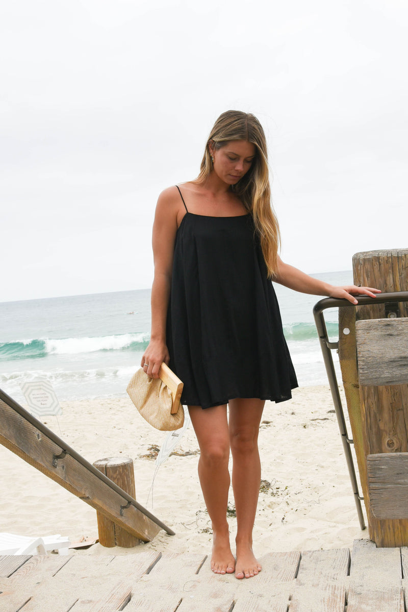 Woman in a black dress standing on a beach with ocean view